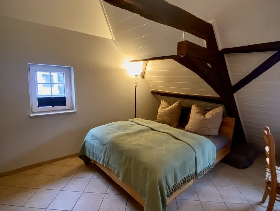 In der Dachgeschoss-Ferienwohnung ist ein Doppelbett, ein TV und ein Schlafsessel vorhanden.